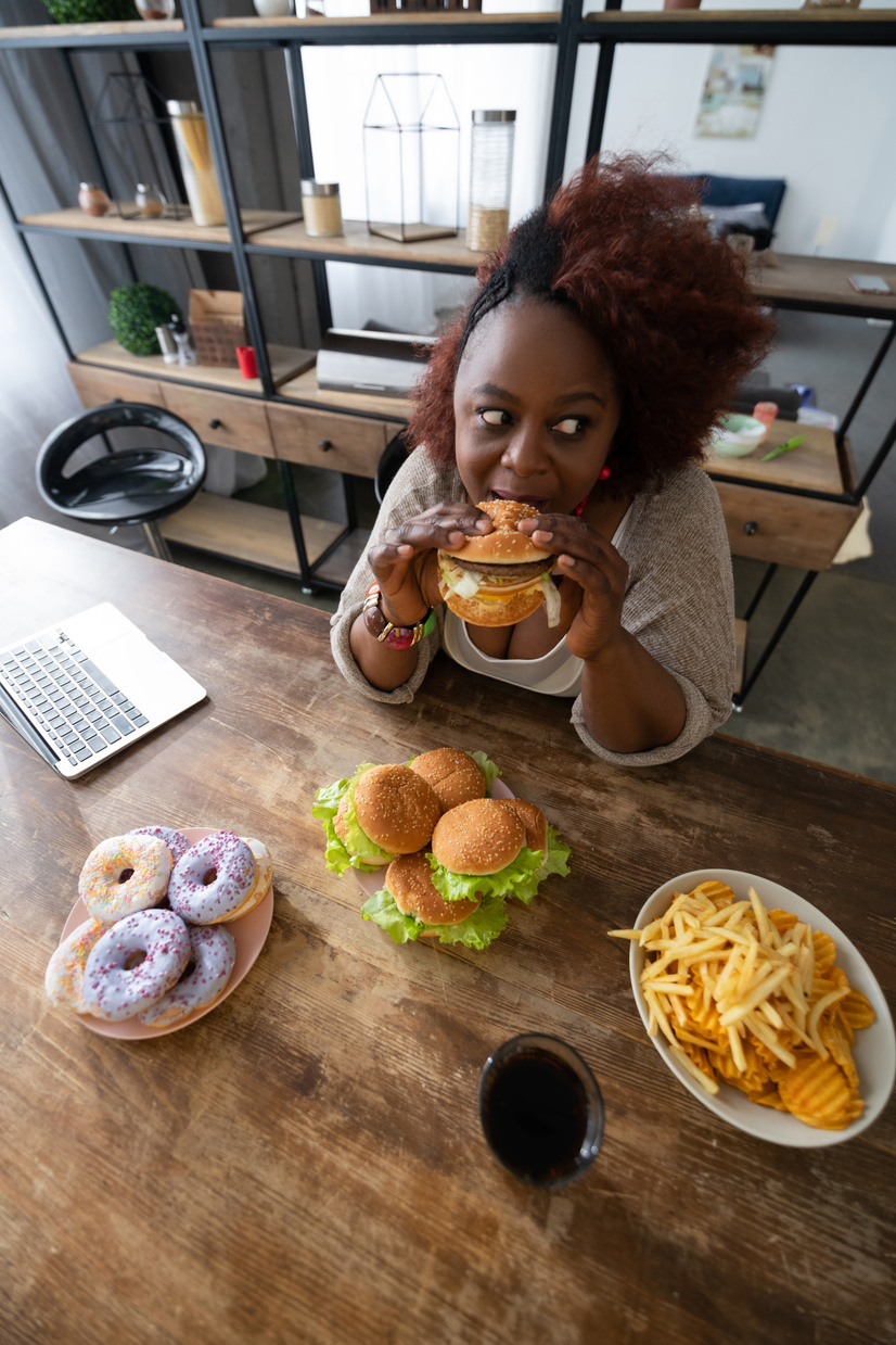 Emotional curly haired female eating junk food